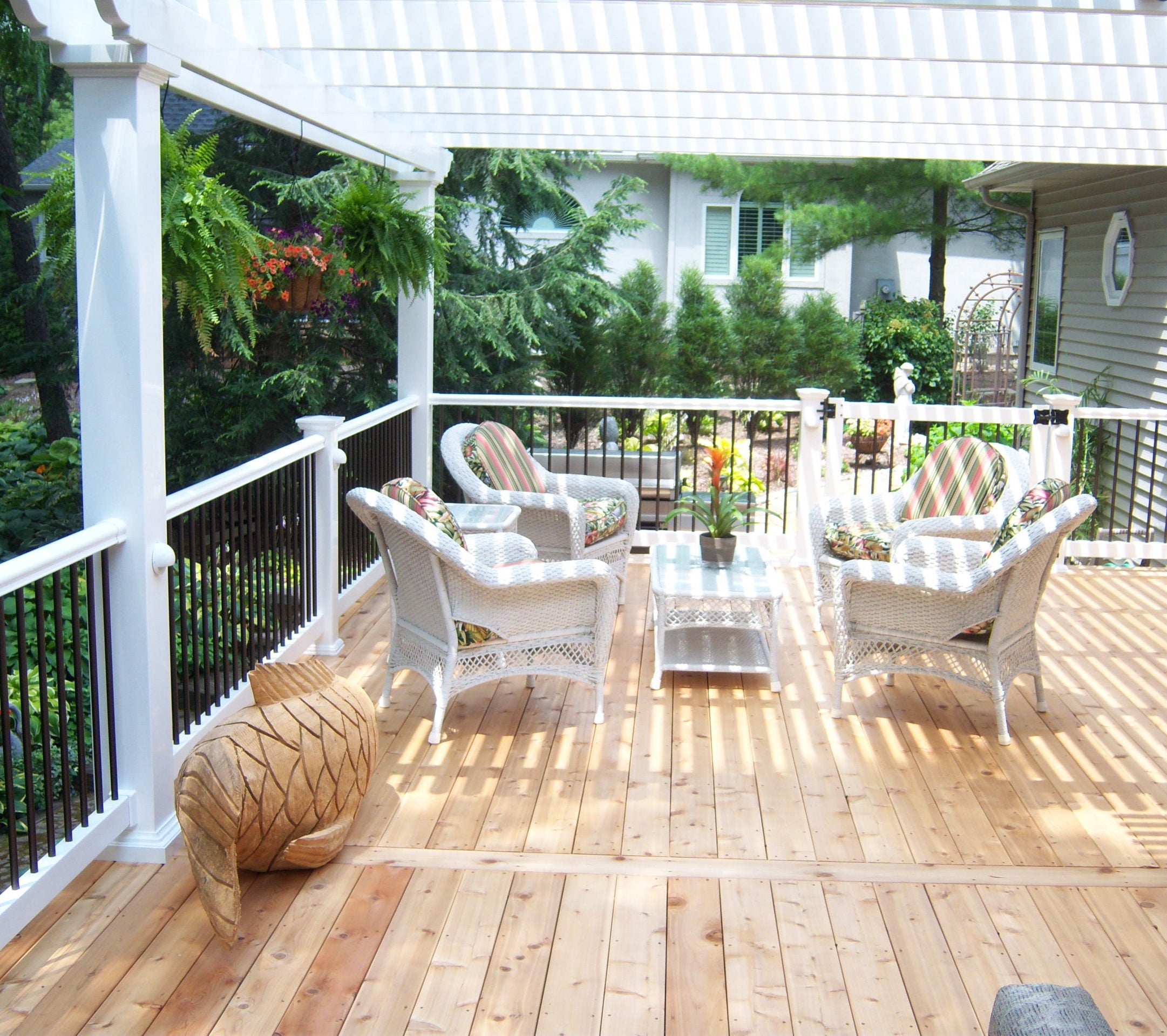 A view from underneath a white traditional pergola covering a wooden deck with a nice railing around it and patio furniture in view