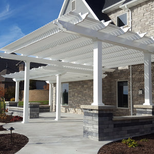 Picture of 2 side-by-side pergolas providing shade for a large L-shaped cement patio area behind a large 2-story stone house