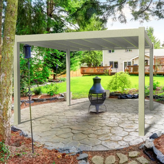 Picture of a 4-post tan modern pergola covering a circular-shaped stone patio surrounded by tall trees with a tan house far in the distance
