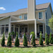 Picture of a white vinyl 2-post modern pergola attached to the corner of a home with an electric fireplace and several trees in the foreground