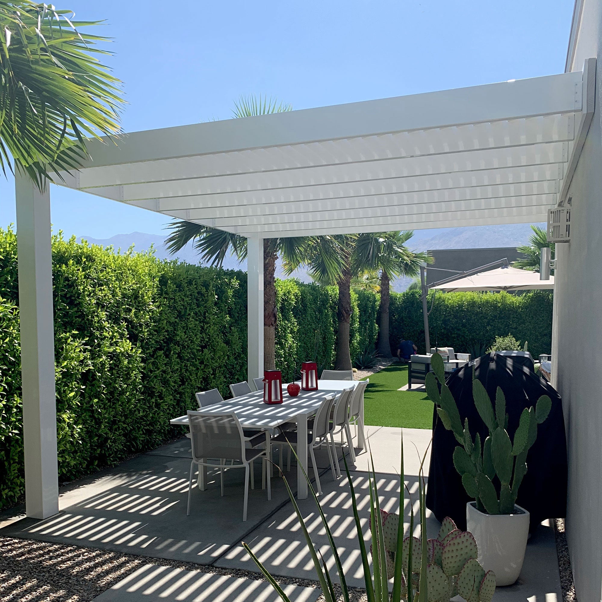 2-post white vinyl modern pergola attached to the side of a house providing shade for an outdoor dining set