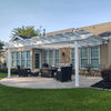 Side view of a traditional white attached pergola with 2 posts and 8 rafters covering a backyard patio with several pieces of patio furniture