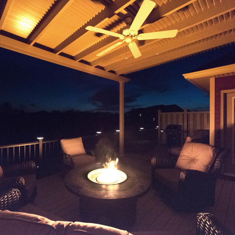 Nighttime view from underneath a pergola with a gas fireplace burning and providing light for the patio and anyone sitting on the patio furniture
