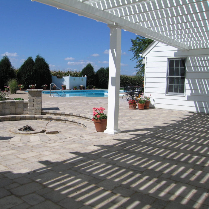 Picture taken underneath a white traditional pergola attached to a white house near a nice circular firepit and a swimming pool in the background