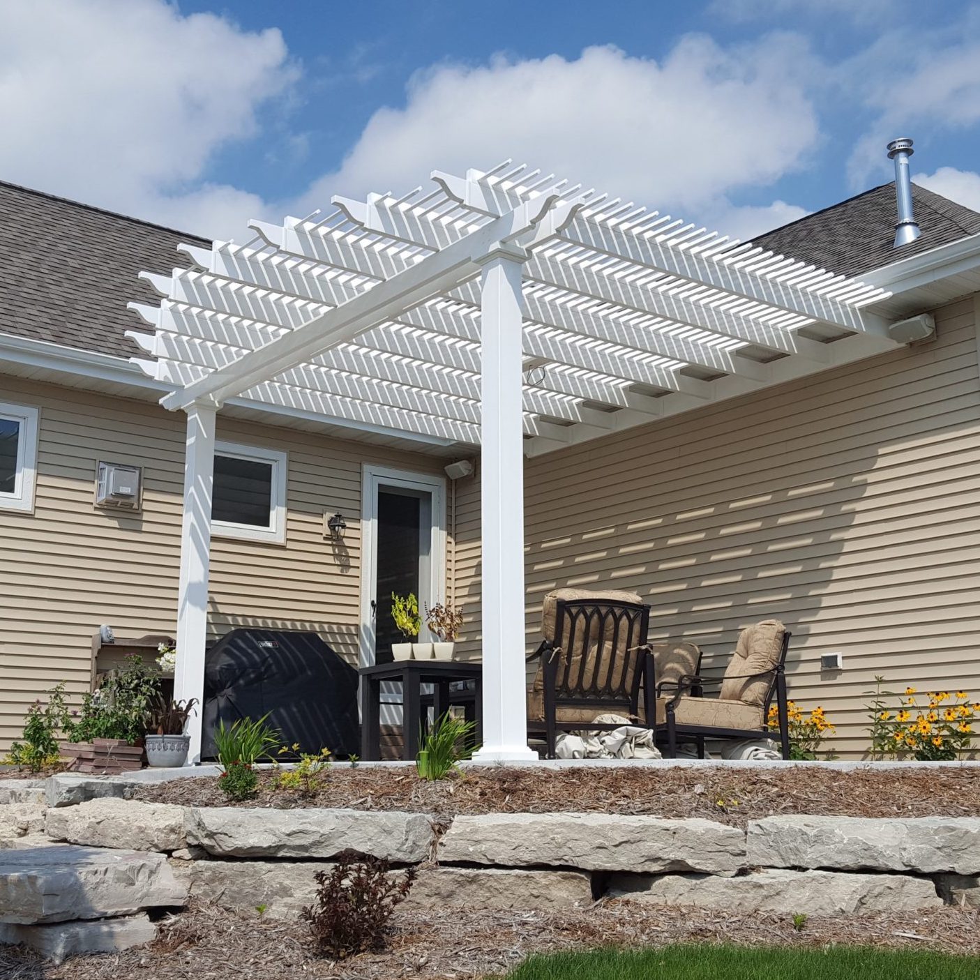 Picture of a white 2-post traditional pergola with overhangs covering the back patio of a home with different length rafters giving the pergola roof a semi-circle shape 