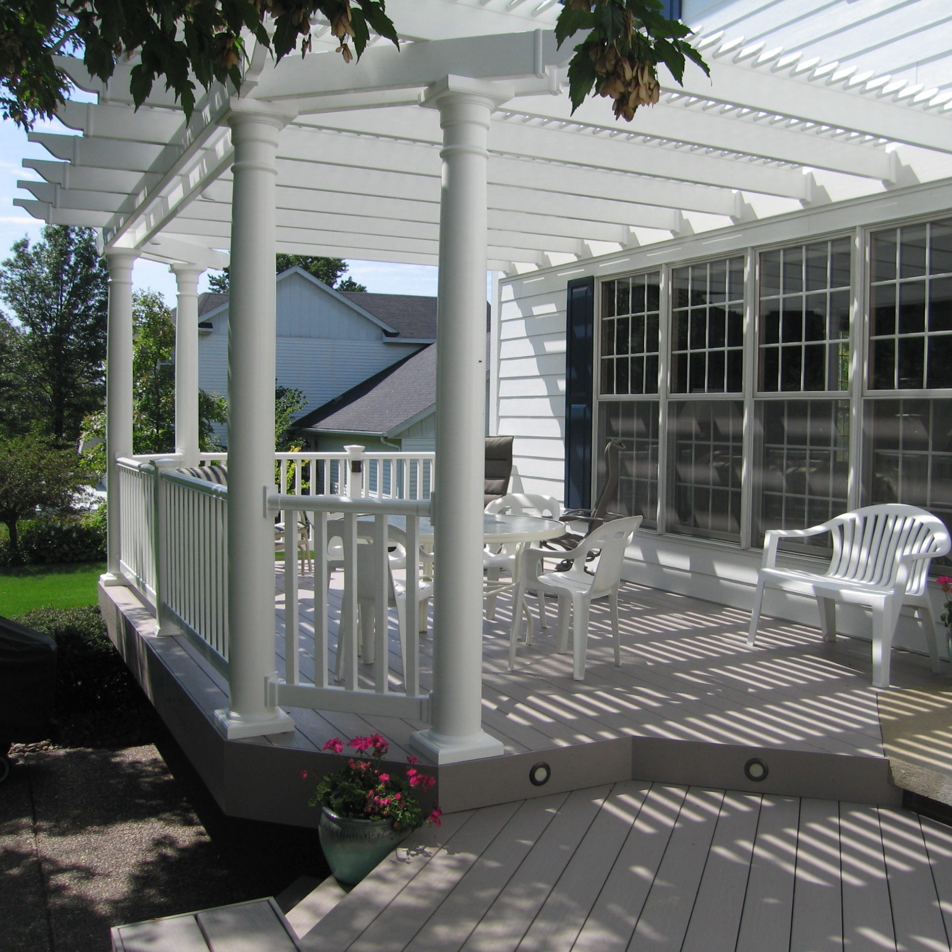 Picture of a white attached traditional pergola with 4 round posts and angled corners covering the patio just off a house with many windows