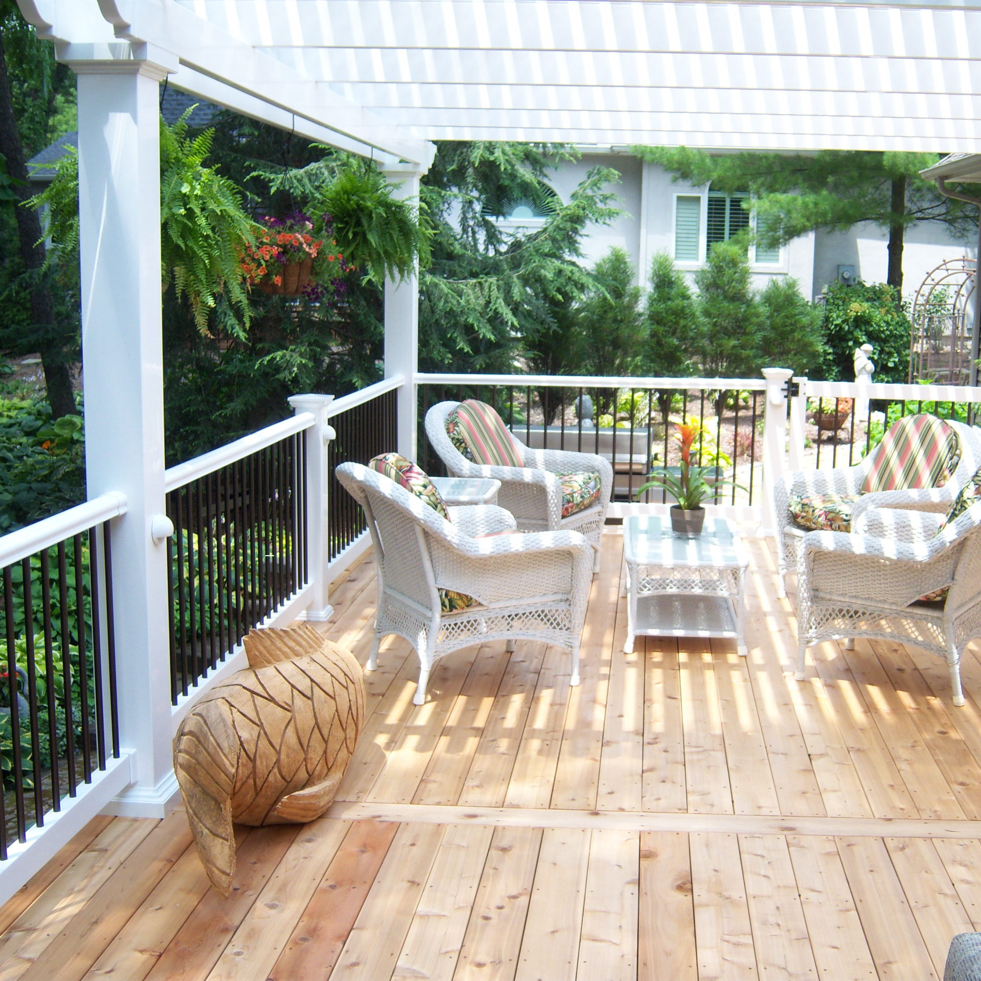 Picture taken underneath a house-attached pergola covering a beautiful wood deck with patio furniture