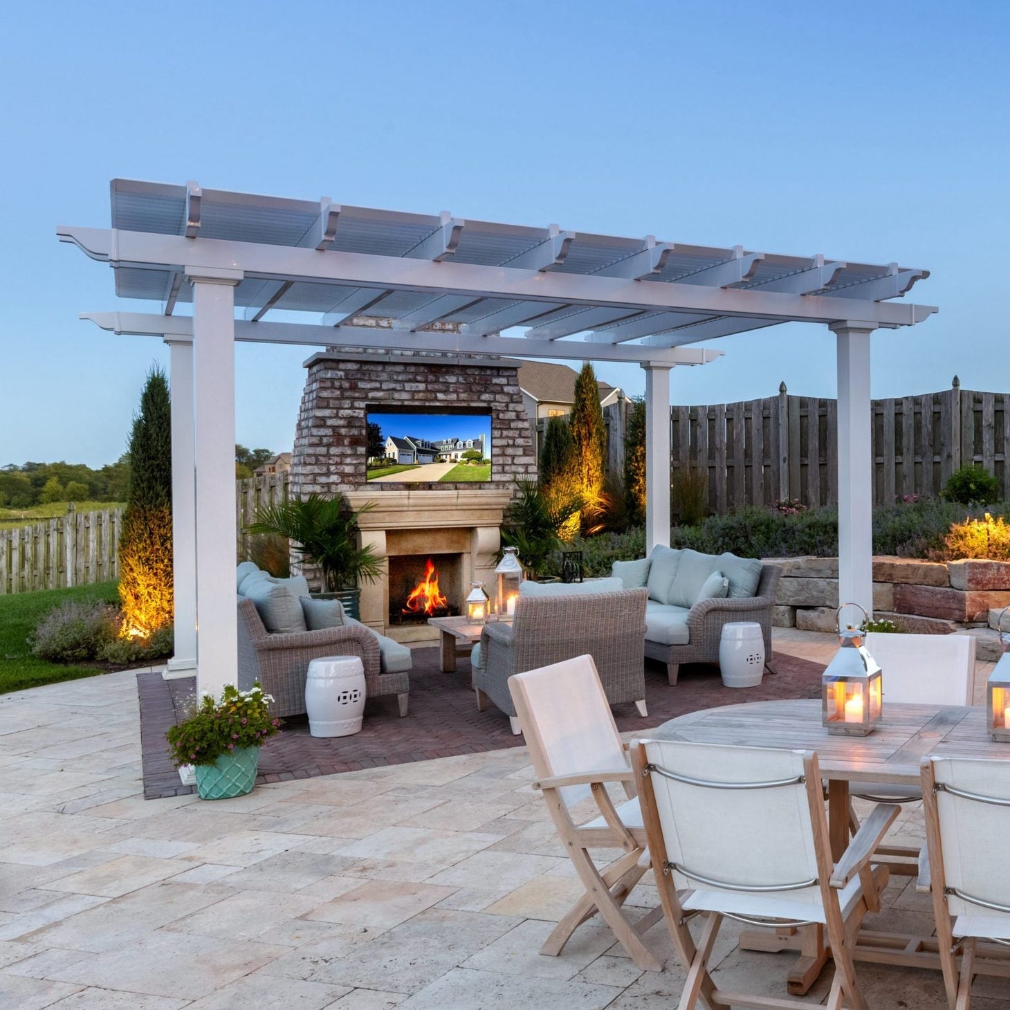 Picture of a white 4-post traditional pergola with overhangs covering several outdoor couches next to a tall brick fireplace and TV