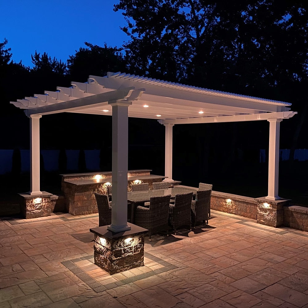 Nighttime view of a 4-post free-standing pergola over an outdoor dining set with lights around the pergola and built into the roof of the pergola