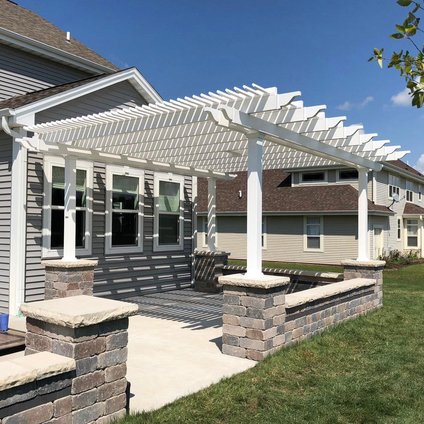 White 4-post traditional pergola with overhangs providing shade for patio near a beautiful house