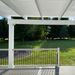 Picture taken from underneath a white vinyl pergola covering a trex deck with grass and trees in the background