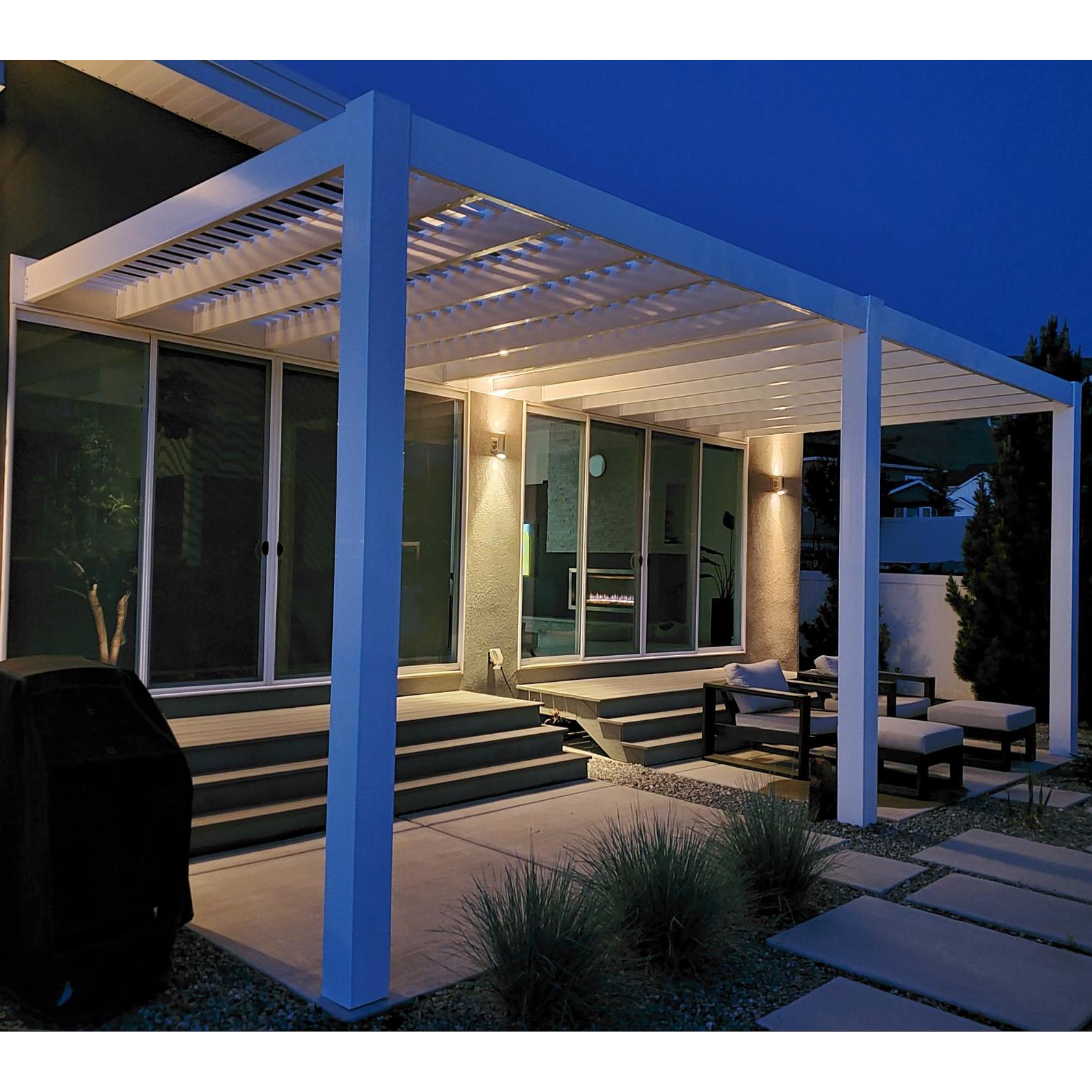 Nighttime view of a white modern attached 3-post pergola covering a 2-part patio behind a stucco home